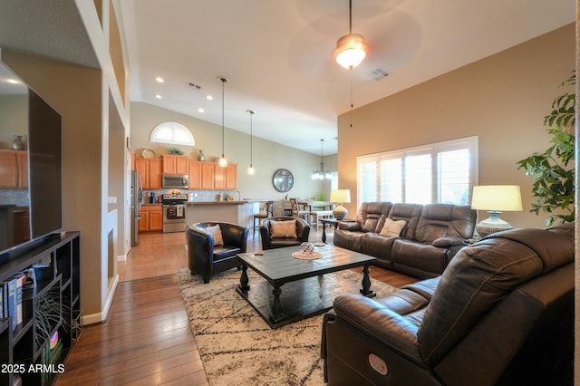 living room featuring high vaulted ceiling, visible vents, light wood finished floors, and ceiling fan with notable chandelier