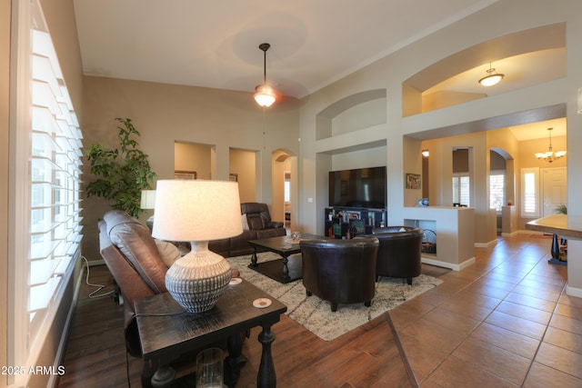 living area featuring baseboards, arched walkways, tile patterned floors, a high ceiling, and a chandelier