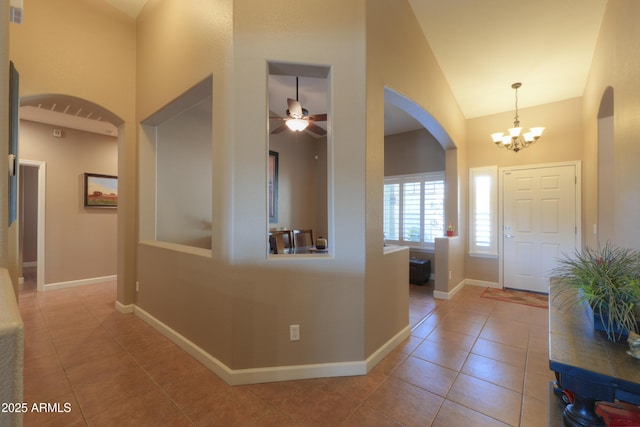 foyer featuring high vaulted ceiling, ceiling fan with notable chandelier, baseboards, and tile patterned floors