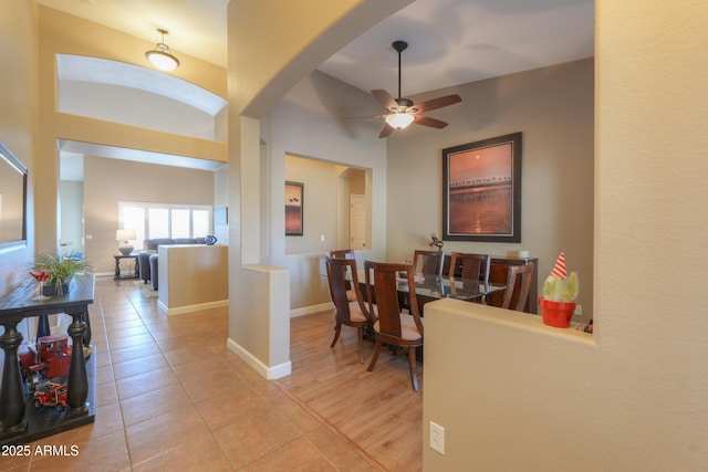 dining area featuring a towering ceiling, light tile patterned floors, baseboards, and a ceiling fan