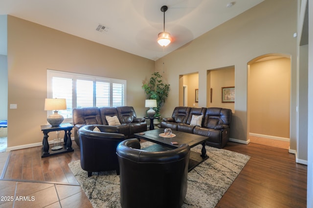 living area with arched walkways, visible vents, dark wood-type flooring, high vaulted ceiling, and baseboards