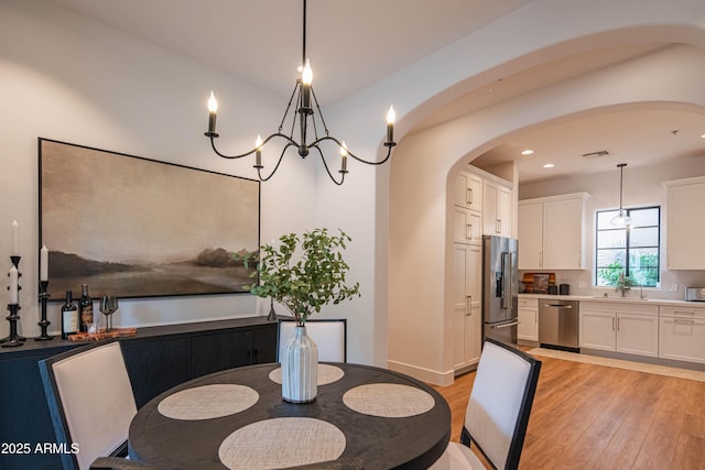 dining area with light wood-type flooring, sink, and a chandelier