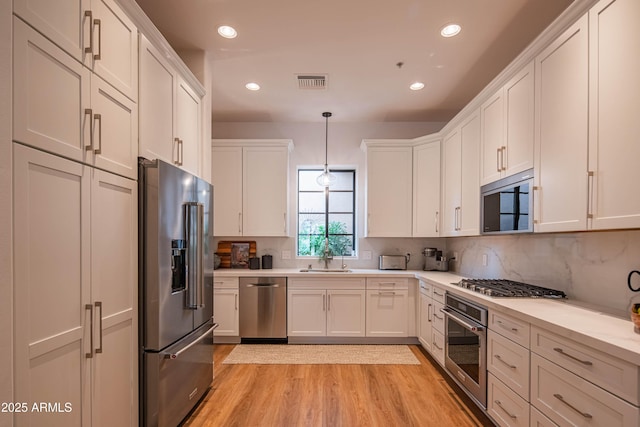 kitchen featuring appliances with stainless steel finishes, tasteful backsplash, decorative light fixtures, light hardwood / wood-style flooring, and sink