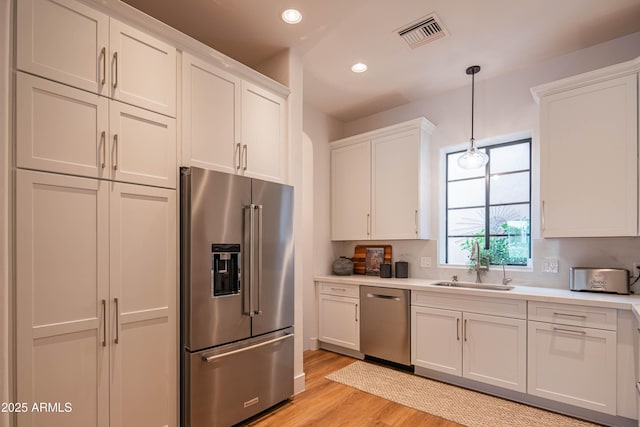 kitchen with white cabinetry, sink, stainless steel appliances, and pendant lighting