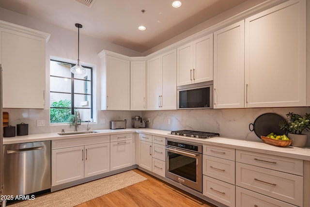 kitchen with hanging light fixtures, white cabinets, sink, and stainless steel appliances