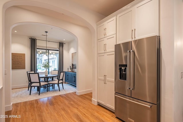 kitchen featuring pendant lighting, high quality fridge, white cabinets, light hardwood / wood-style floors, and a notable chandelier