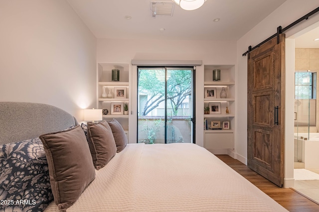 bedroom with ensuite bath, a barn door, and hardwood / wood-style floors