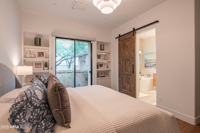 bedroom with access to outside, a barn door, wood-type flooring, and ensuite bath