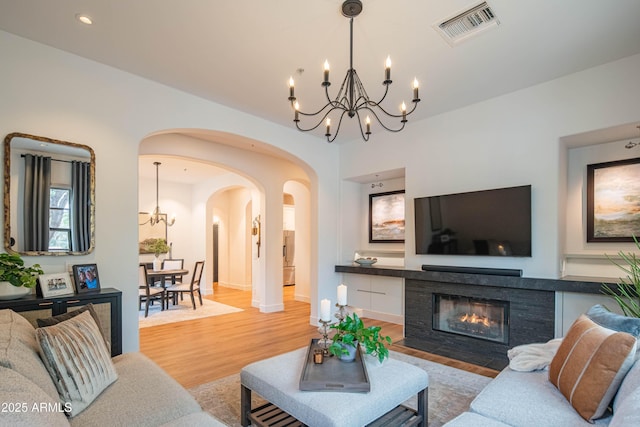 living room featuring light wood-type flooring, a chandelier, and a tile fireplace