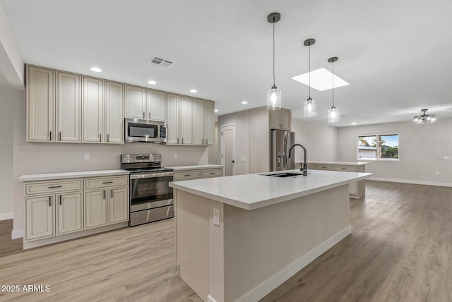 kitchen featuring light hardwood / wood-style flooring, pendant lighting, stainless steel appliances, cream cabinets, and a kitchen island with sink