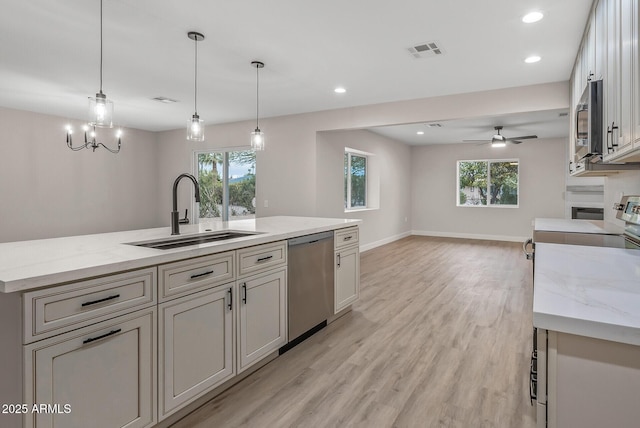 kitchen featuring a kitchen island with sink, decorative light fixtures, light stone countertops, sink, and appliances with stainless steel finishes