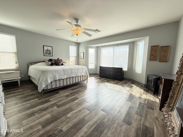 bedroom with baseboards, visible vents, a ceiling fan, dark wood-style floors, and a wood stove