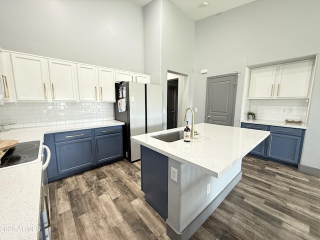 kitchen with blue cabinetry, freestanding refrigerator, white cabinetry, a sink, and a kitchen island with sink