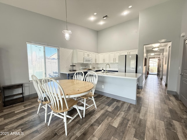 kitchen featuring light countertops, visible vents, white microwave, freestanding refrigerator, and white cabinets