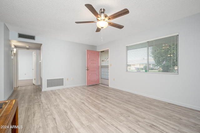 empty room featuring a textured ceiling, light wood-type flooring, and ceiling fan