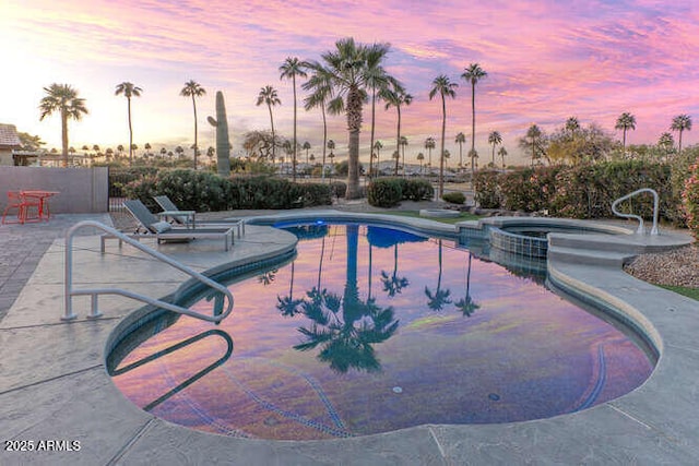 pool at dusk featuring an in ground hot tub and a patio