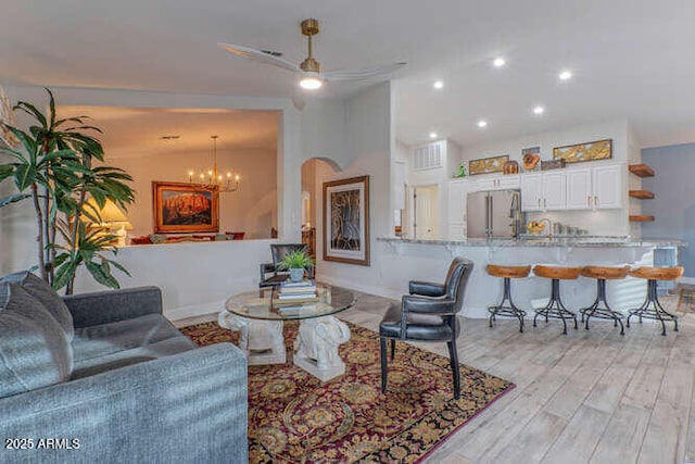 living room featuring ceiling fan with notable chandelier and light wood-type flooring