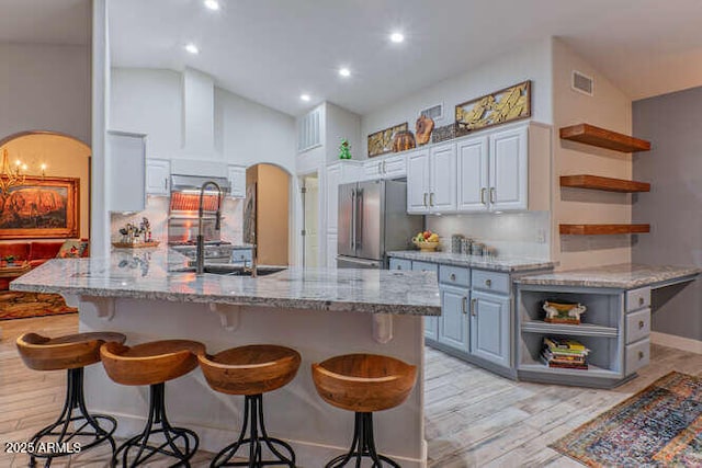 kitchen featuring stainless steel refrigerator, backsplash, a kitchen breakfast bar, light stone countertops, and light hardwood / wood-style floors