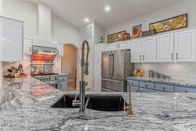 kitchen with sink, white cabinetry, light stone counters, high end appliances, and tasteful backsplash