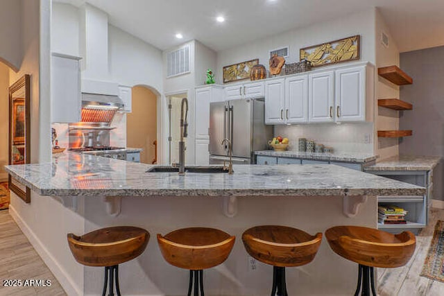 kitchen with high end fridge, light stone counters, light wood-type flooring, decorative backsplash, and white cabinets