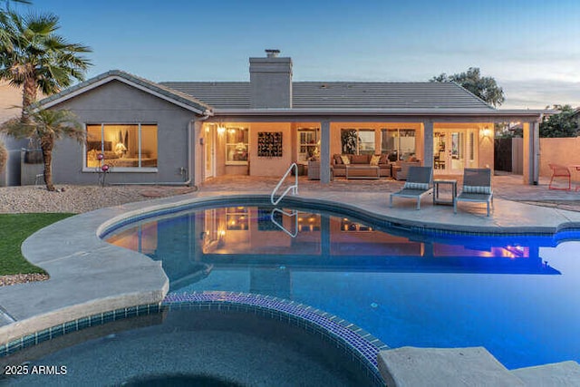 pool at dusk featuring an in ground hot tub, outdoor lounge area, and a patio