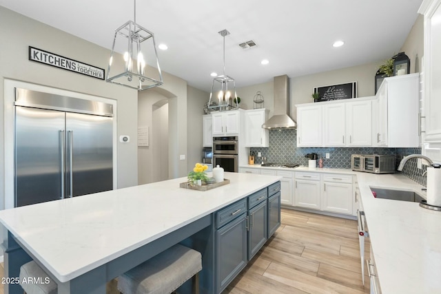 kitchen with a sink, visible vents, white cabinetry, and wall chimney range hood