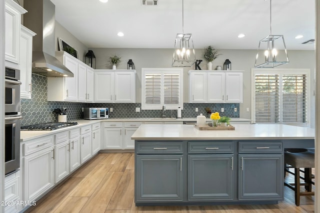 kitchen featuring gray cabinets, white cabinetry, light countertops, and wall chimney range hood