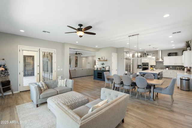 living room with ceiling fan with notable chandelier, recessed lighting, light wood-style floors, and visible vents