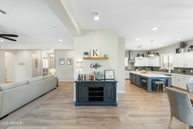 kitchen featuring white cabinetry, decorative backsplash, wall chimney exhaust hood, and open floor plan