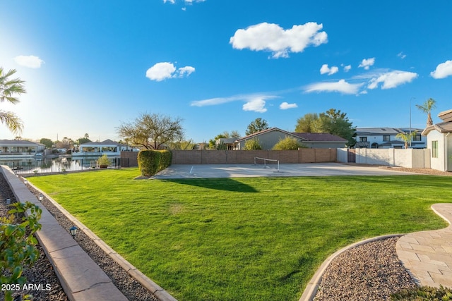 view of yard with basketball court, a residential view, a water view, and fence