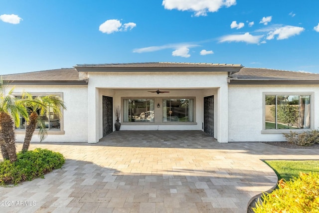 rear view of house featuring ceiling fan and stucco siding