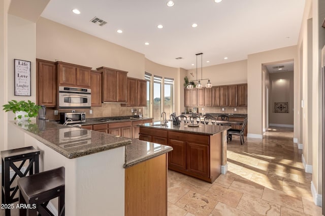 kitchen with tasteful backsplash, appliances with stainless steel finishes, kitchen peninsula, a kitchen island, and pendant lighting