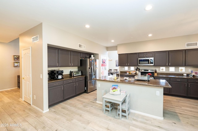 2224 W Olive Way, Chandler, AZ 85248 - kitchen featuring appliances with stainless steel finishes, dark stone counters, light wood-style flooring, recessed lighting, and a kitchen island with sink