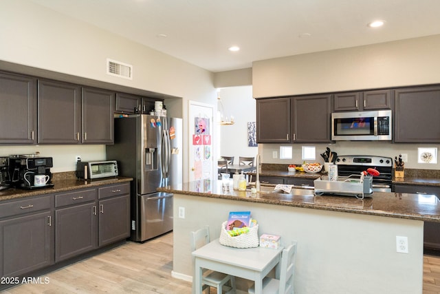 2224 W Olive Way, Chandler, AZ 85248 - kitchen featuring appliances with stainless steel finishes, dark stone countertops, light wood-style flooring, a kitchen island with sink, and recessed lighting