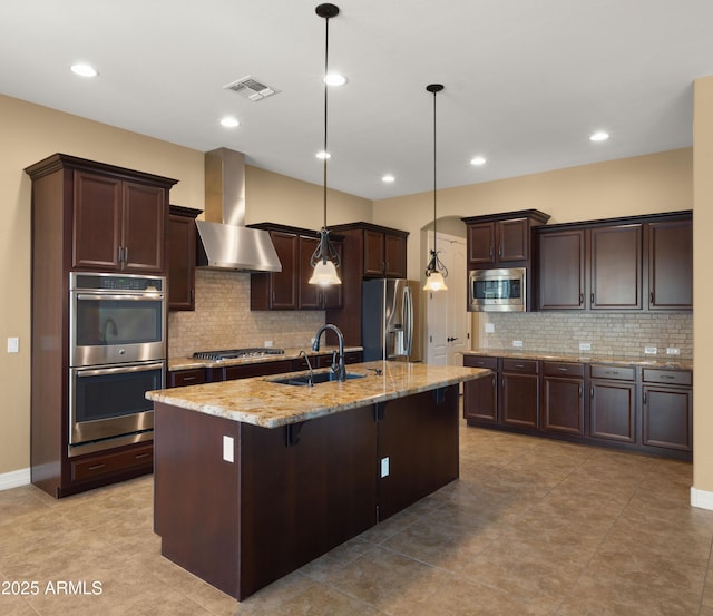 kitchen with visible vents, dark brown cabinetry, appliances with stainless steel finishes, wall chimney exhaust hood, and a sink