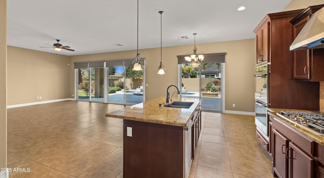 kitchen featuring a kitchen island with sink, a sink, appliances with stainless steel finishes, under cabinet range hood, and ceiling fan with notable chandelier