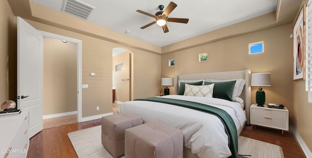 bedroom with visible vents, wood finished floors, arched walkways, baseboards, and ceiling fan