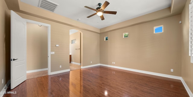 spare room with wood finished floors, baseboards, visible vents, arched walkways, and ceiling fan