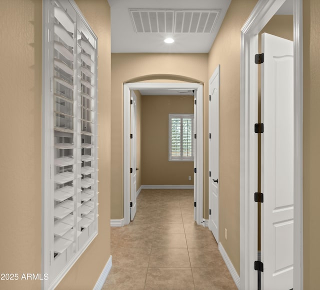 corridor featuring light tile patterned floors, visible vents, arched walkways, and baseboards