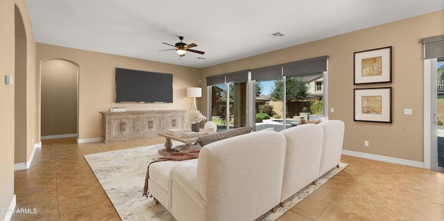 living area with light tile patterned floors, baseboards, arched walkways, and ceiling fan