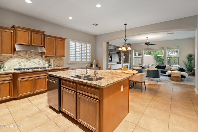 kitchen featuring a kitchen island with sink, ceiling fan with notable chandelier, sink, light stone counters, and stainless steel gas cooktop