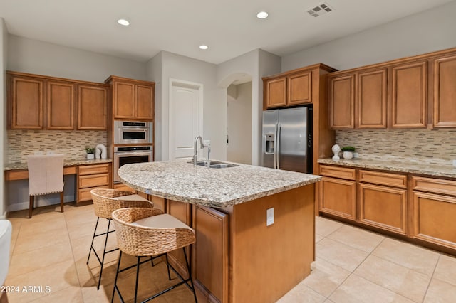 kitchen with sink, tasteful backsplash, light stone counters, an island with sink, and appliances with stainless steel finishes