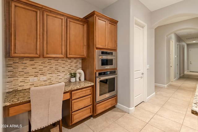 kitchen featuring backsplash, light stone countertops, light tile patterned floors, and built in desk