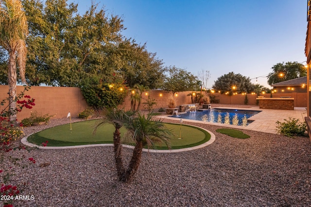 pool at dusk with pool water feature and a patio