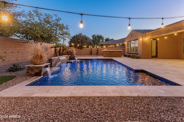 pool at dusk featuring pool water feature and a patio