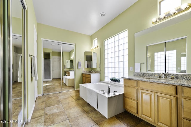 bathroom featuring two vanities, a sink, a garden tub, and baseboards