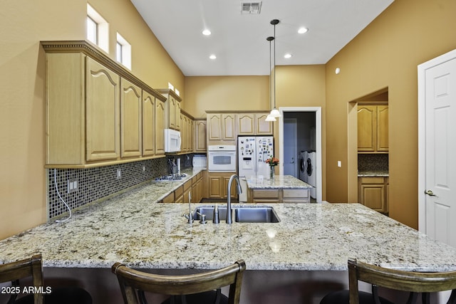 kitchen with white appliances, a peninsula, backsplash, washer and dryer, and a sink
