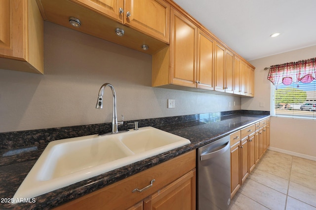 kitchen with light tile patterned floors, a sink, baseboards, stainless steel dishwasher, and dark stone countertops