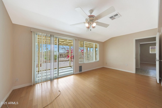 empty room with visible vents, a ceiling fan, vaulted ceiling, light wood-type flooring, and baseboards