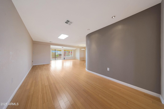 empty room with light wood-type flooring, visible vents, and baseboards